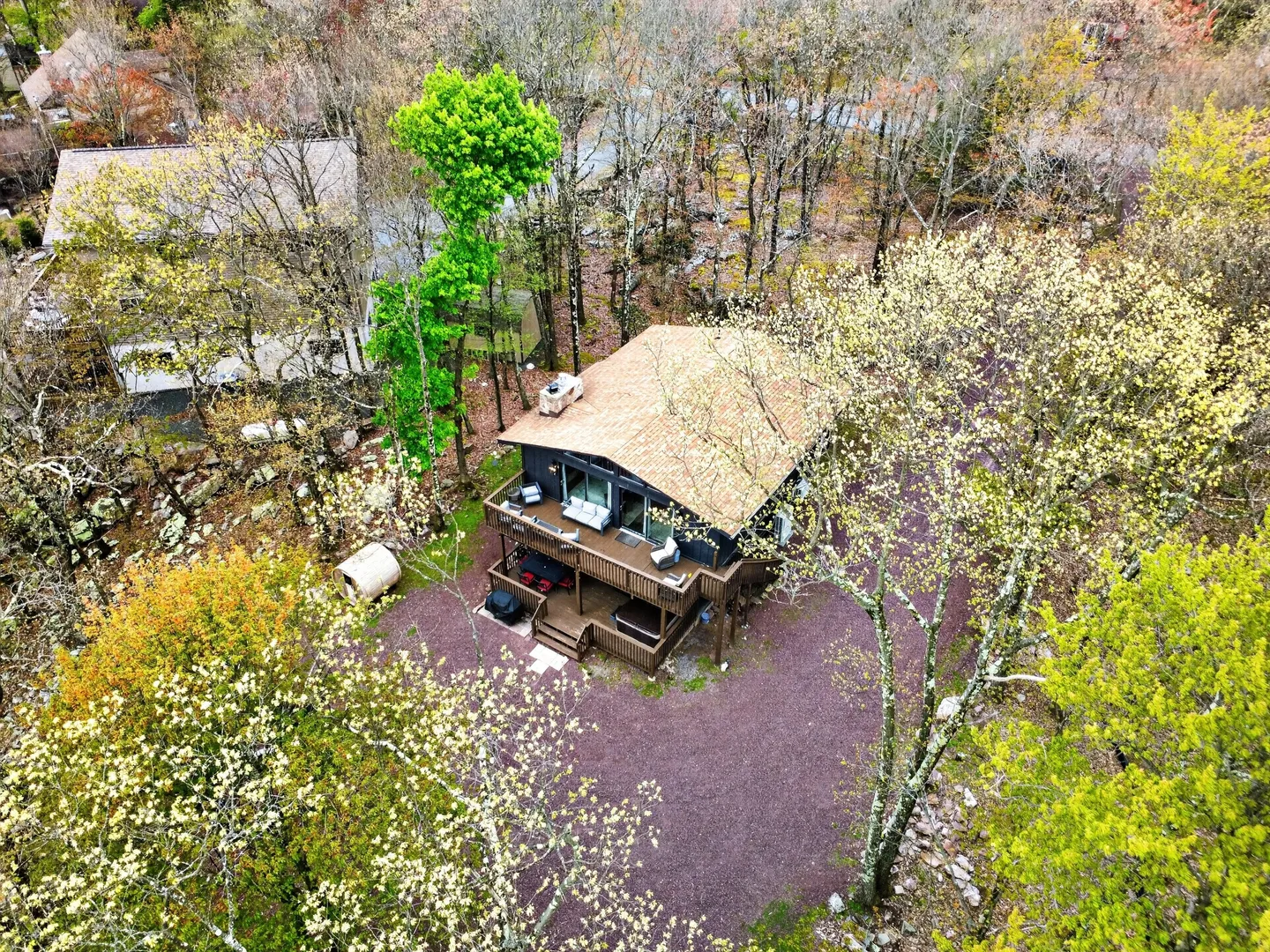 Aerial view of a secluded two-story cabin surrounded by lush trees, featuring a multi-level deck and hot tub.