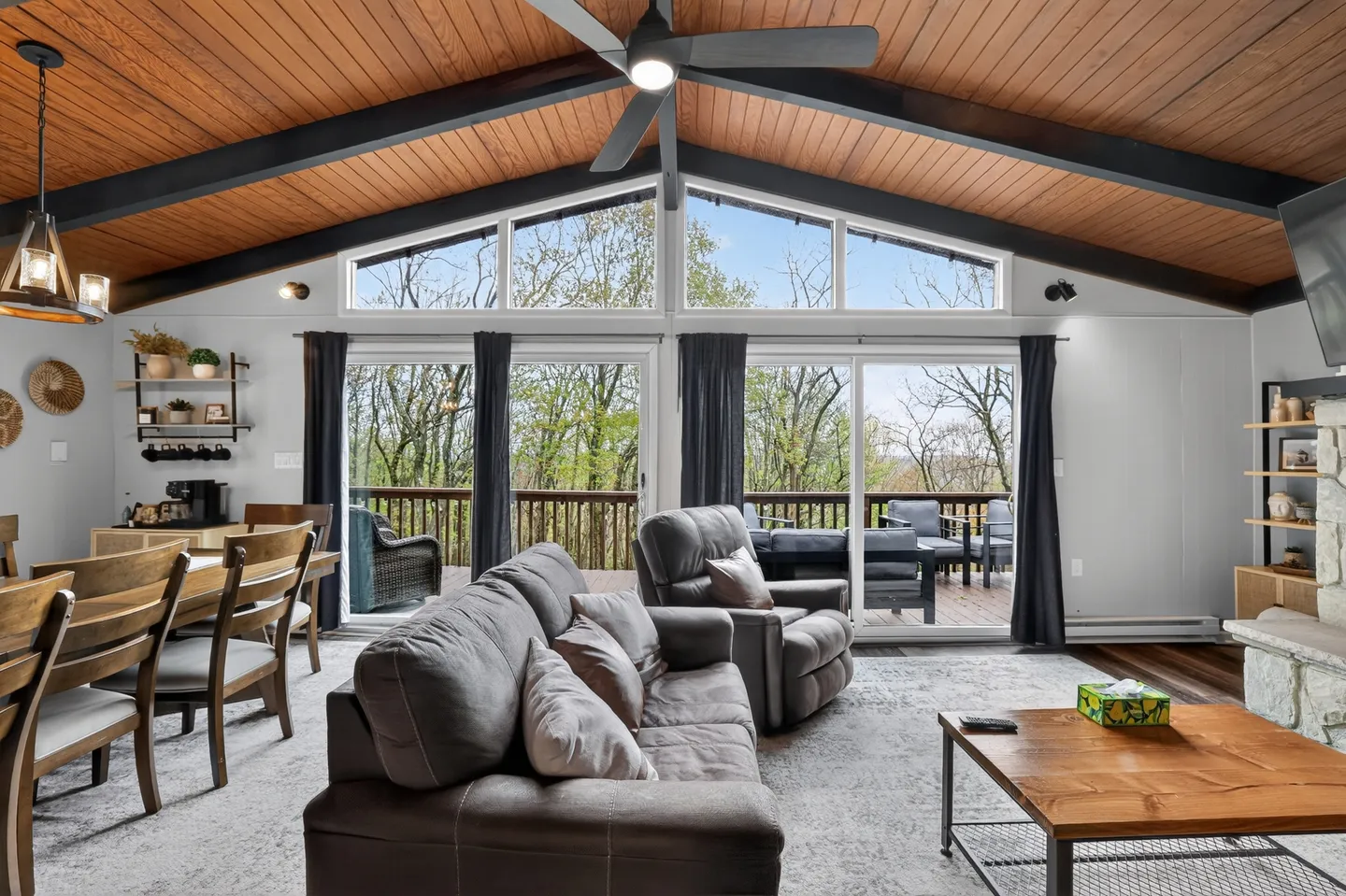 Living and dining area featuring a vaulted wood-paneled ceiling with exposed beams, sliding glass doors to a deck, and comfortable seating.