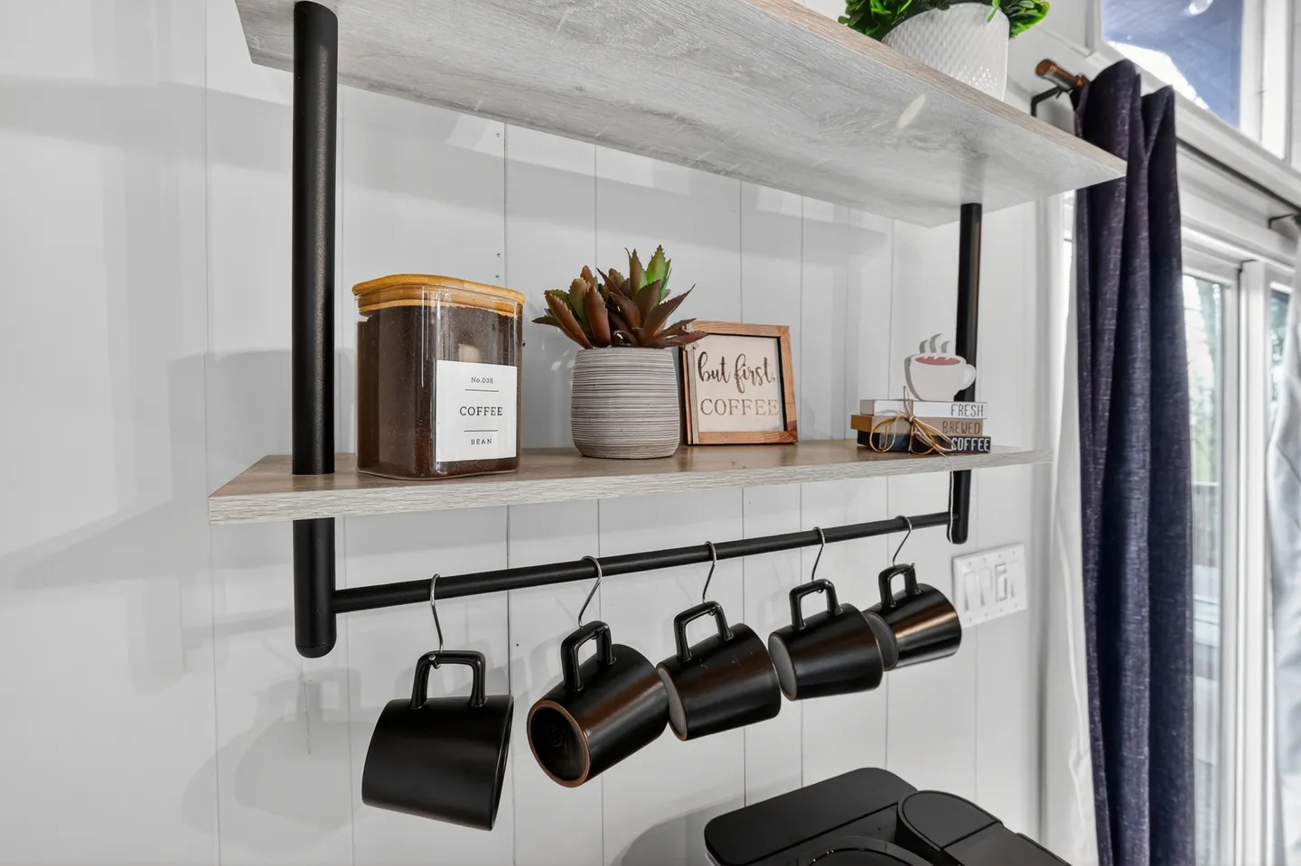Close-up of wall-mounted shelves with coffee mugs hanging underneath a container of coffee beans and decor.