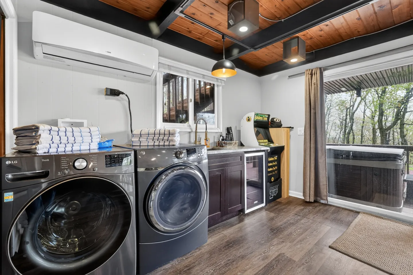 Laundry and utility area with front-load washer and dryer, small wet bar, arcade game, and sliding glass door showing an outdoor hot tub.