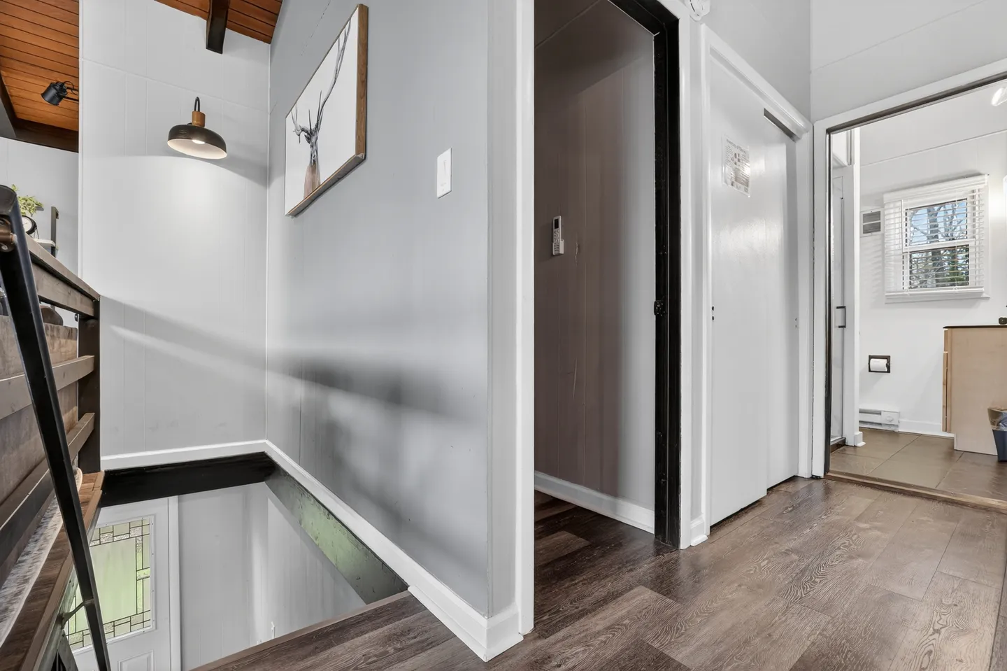 Upstairs hallway with wood-look flooring, light gray walls, a staircase opening with black railing, and doorways leading to other rooms.