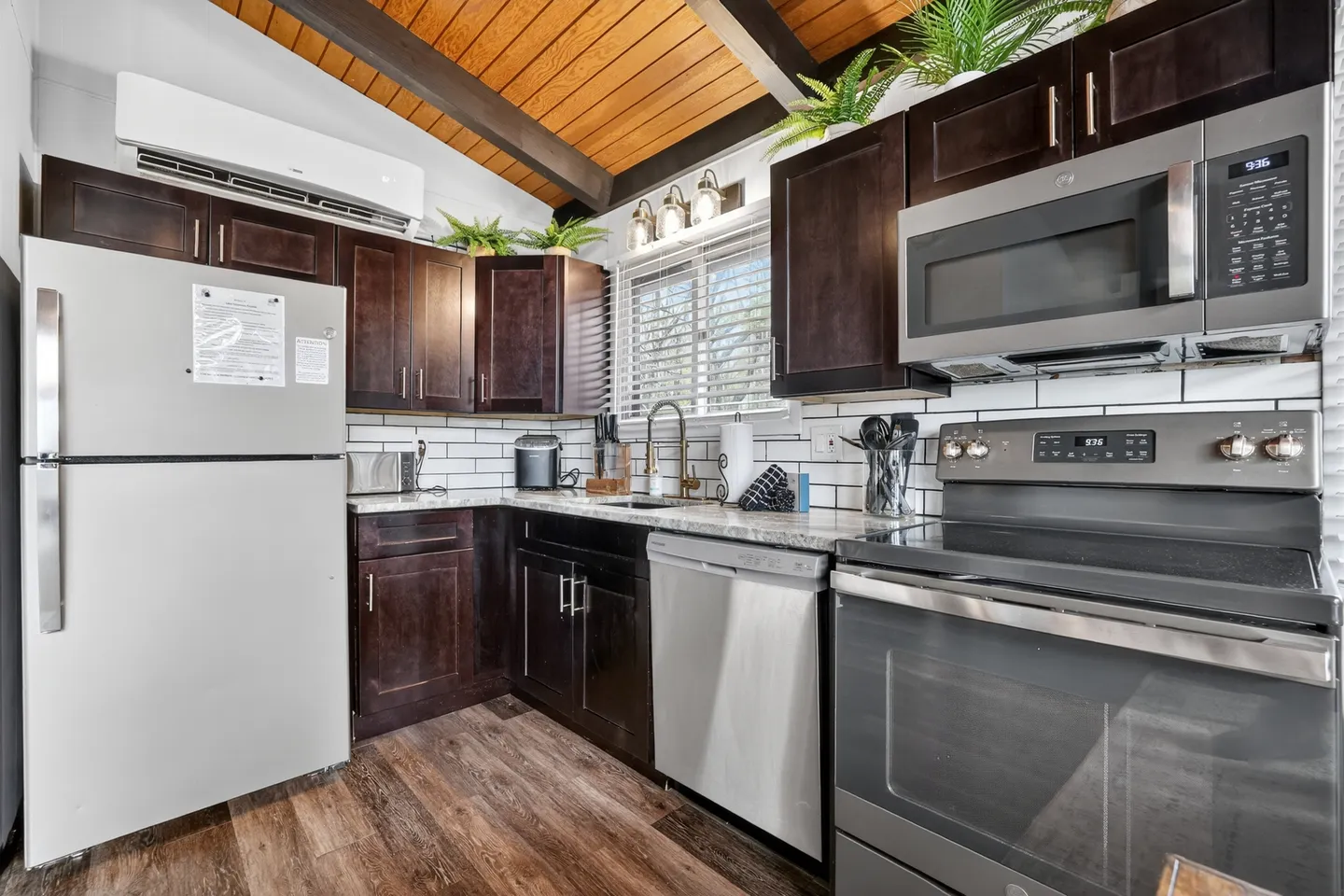 Kitchen with dark cabinetry, stainless steel appliances, a white refrigerator, wood-beam ceiling, and white subway tile backsplash.