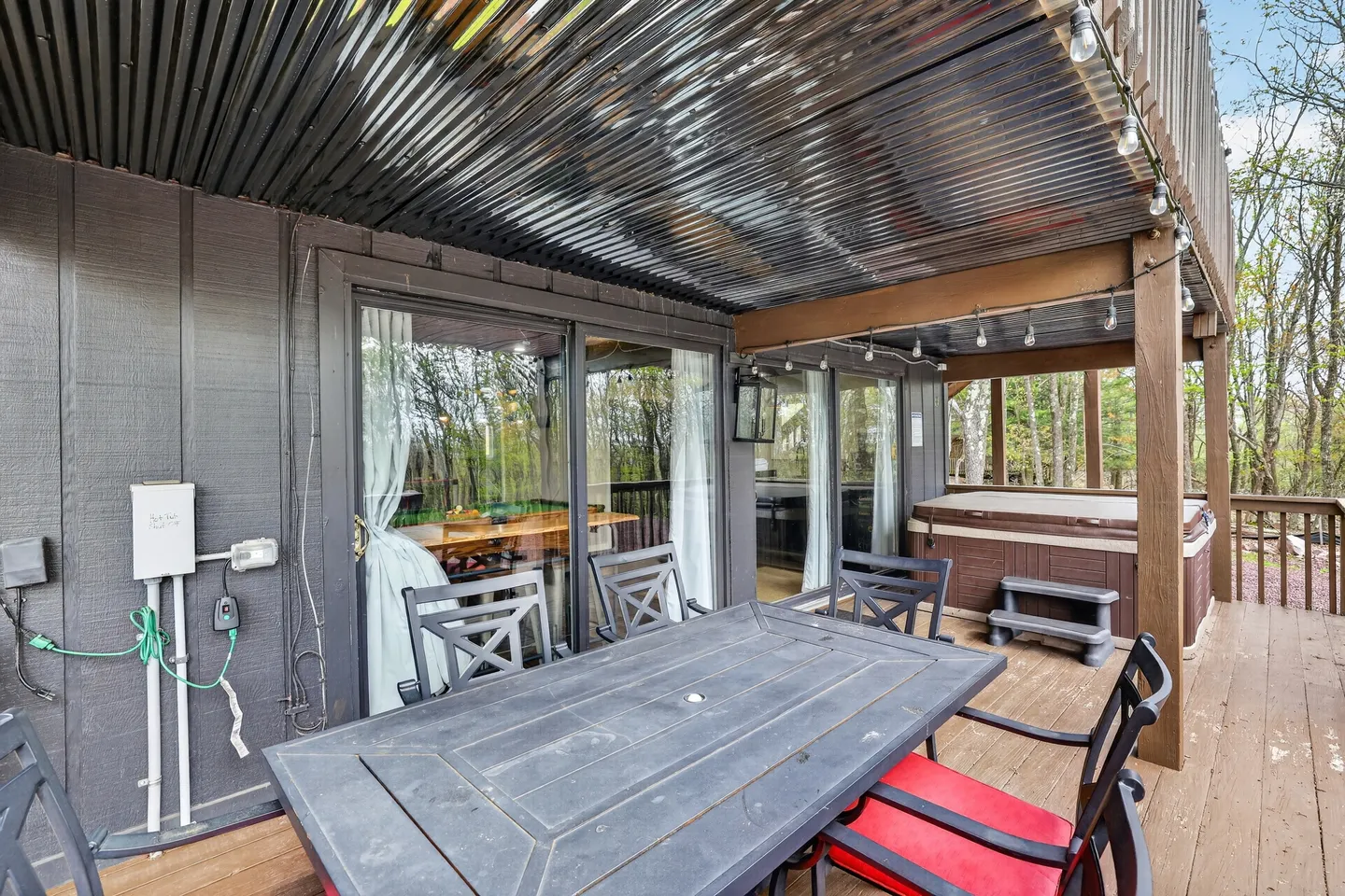 Covered outdoor patio with a dining table, chairs, hot tub, and sliding glass doors leading indoors.