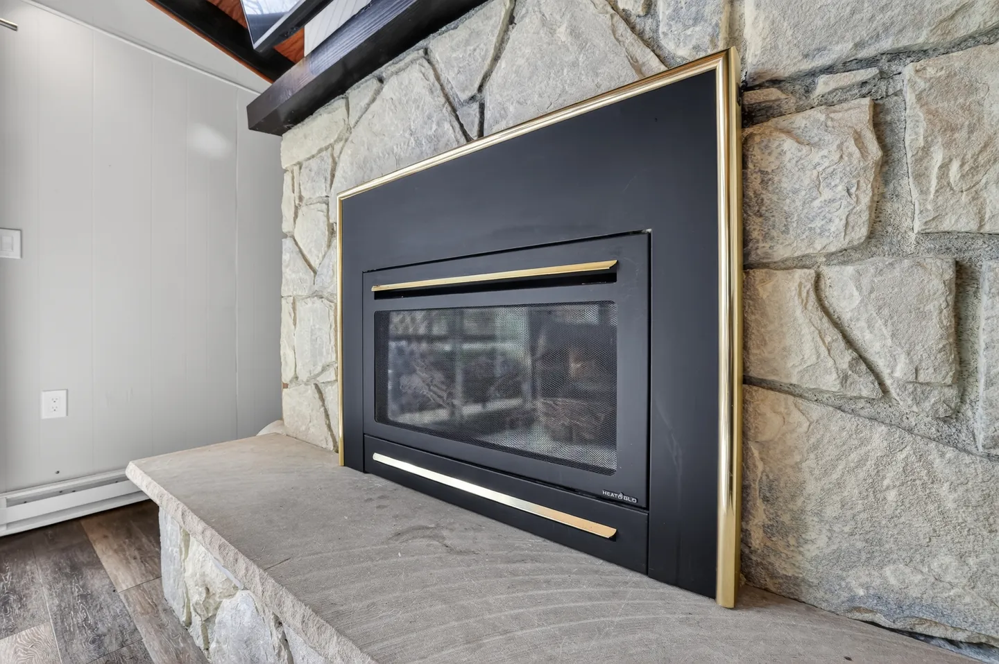 Close-up view of a modern black fireplace insert with gold trim set into a stone fireplace surround and hearth.