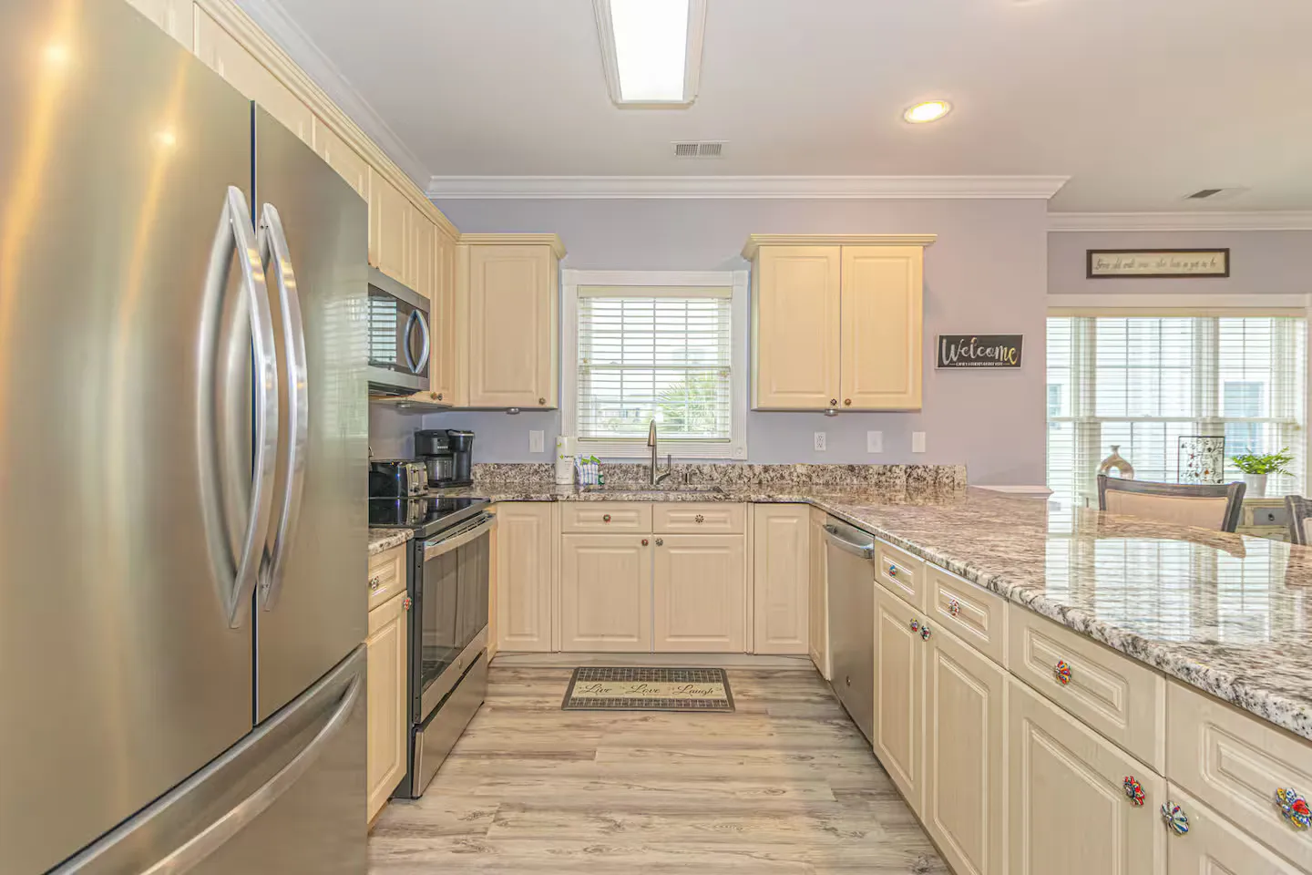 Kitchen with stainless steel appliances, cream-colored cabinetry, mottled granite countertops, and light wood-look flooring.