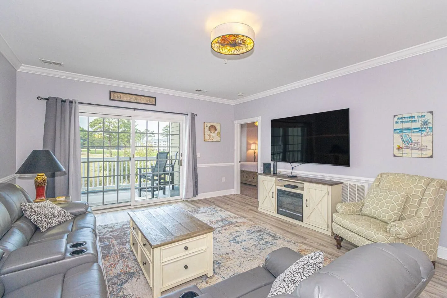 Living room with reclining gray sofas, coffee table, TV mounted above a fireplace console, and sliding doors leading to a screened porch.
