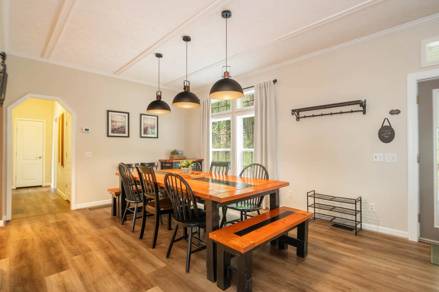 Dining area featuring a long wooden table with black spindle chairs and matching wooden benches under three pendant lights.