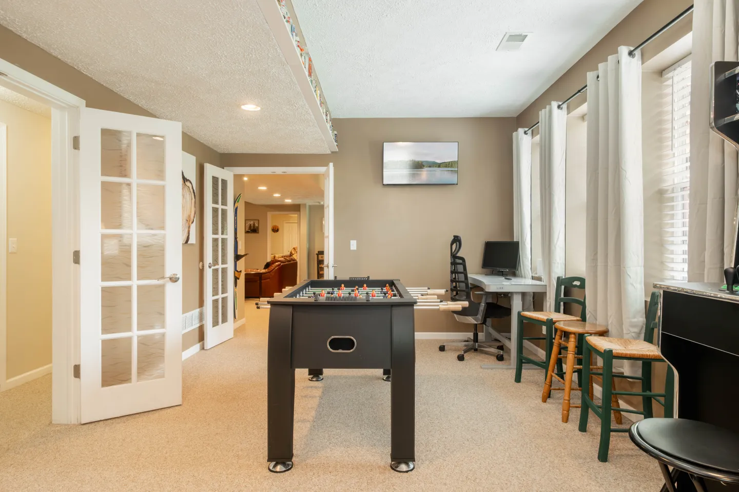 Game room featuring a black foosball table on carpeted flooring, with a computer desk, bar stools, and glass French doors.