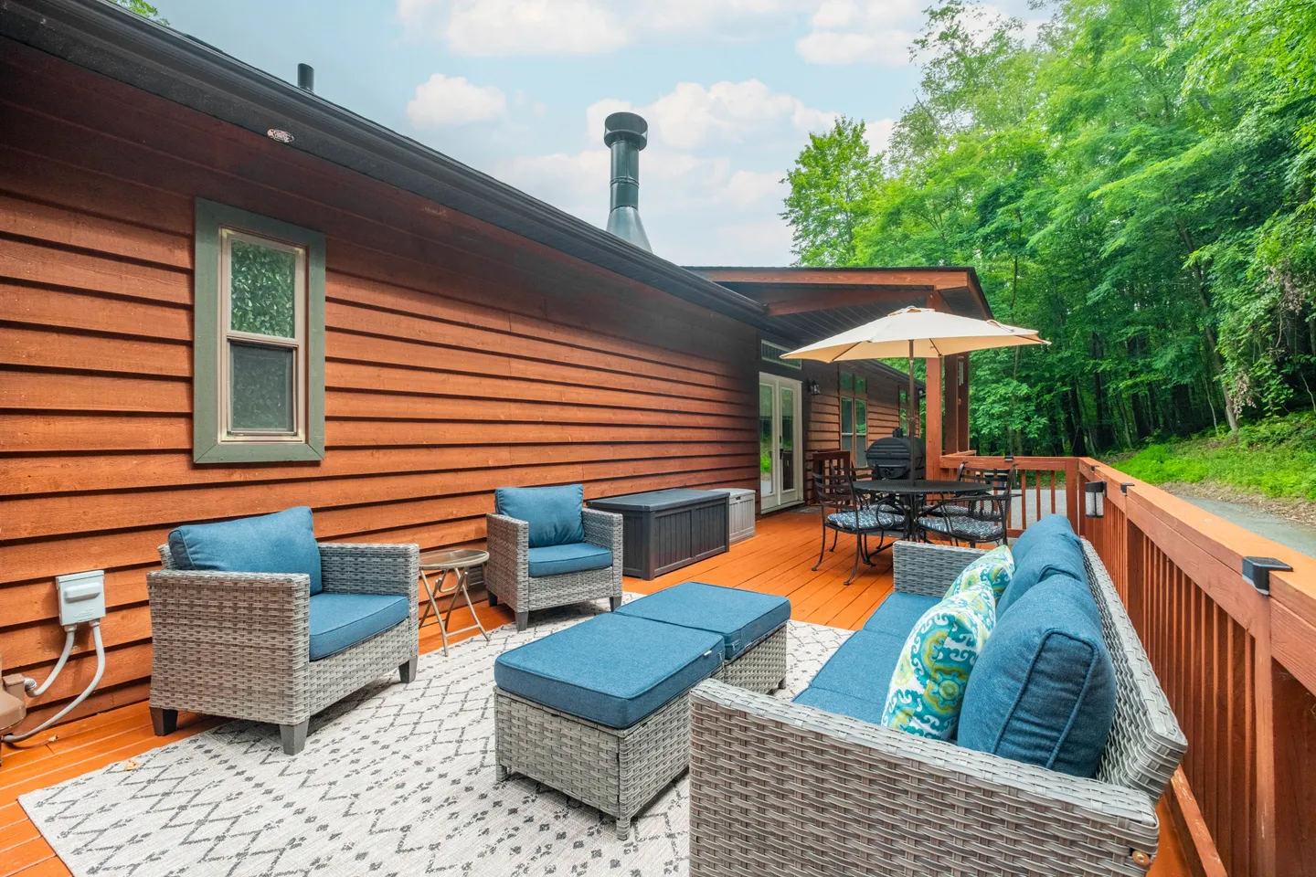 Spacious wood deck with wicker lounge furniture, cushions, an outdoor rug, and a dining set under an umbrella.