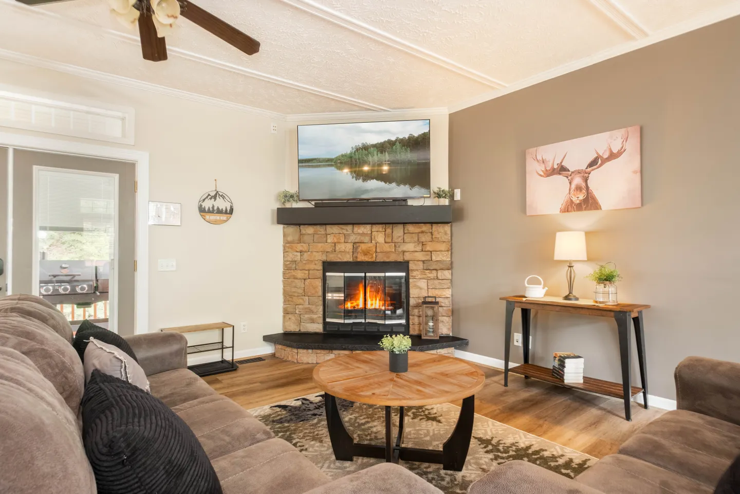 Living room with plush sofas, round coffee table, and a corner stone fireplace beneath a wall-mounted TV.