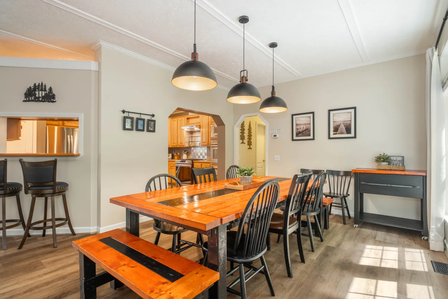 Dining area featuring a long wood dining table with chairs, a matching bench, pendant lights, and a view into the kitchen.
