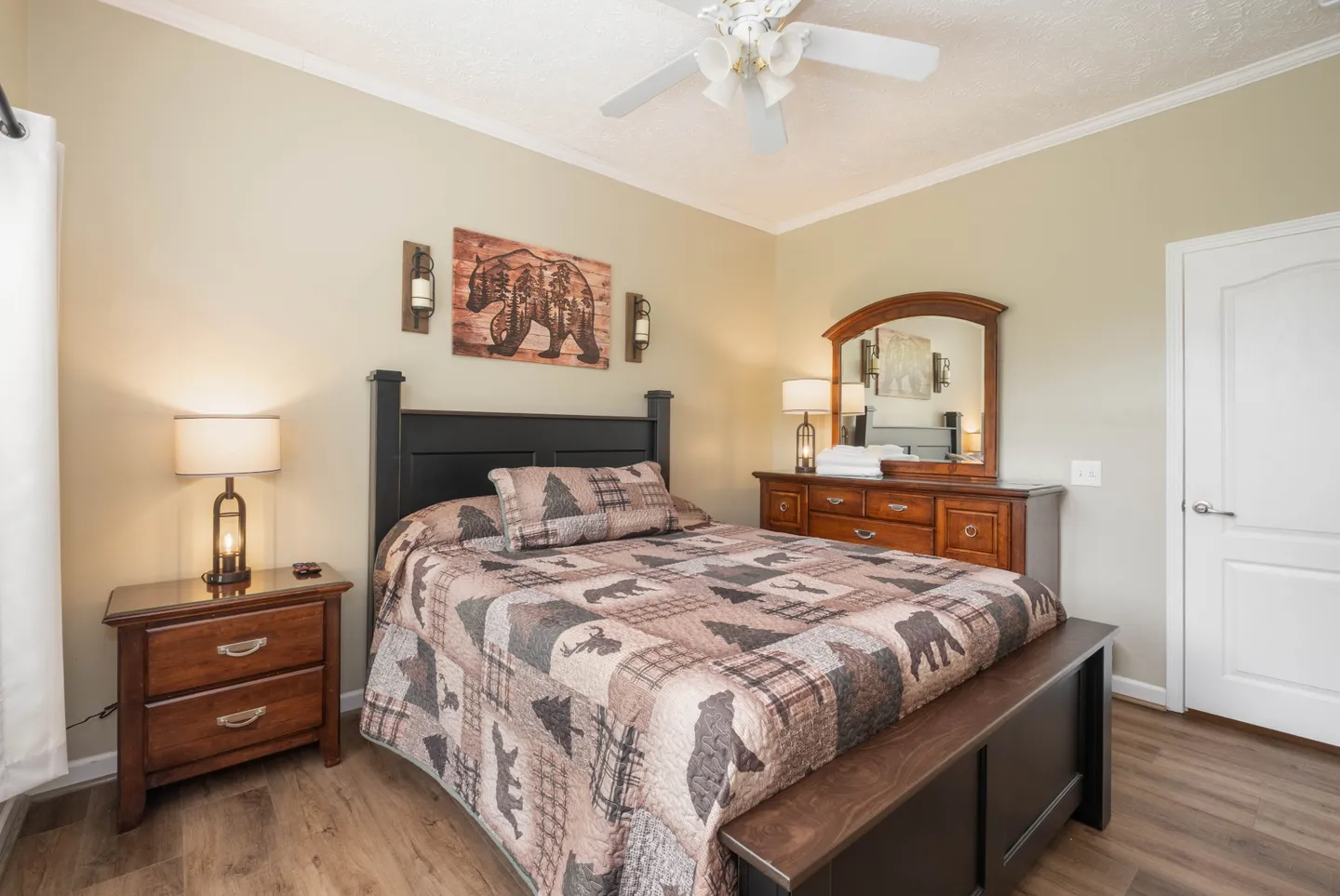 Bedroom with a dark wood bed frame, rustic patterned quilt, wood nightstand with lamp, and matching dresser with mirror.