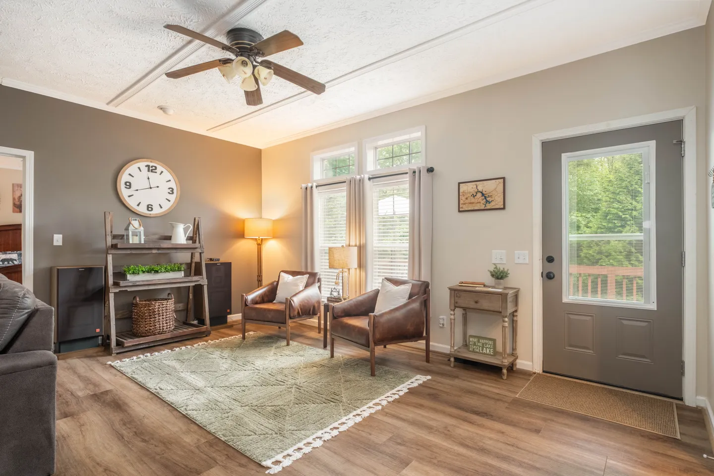 Living room with wood-style flooring, a pair of leather armchairs, an area rug, an entrance door with a window, and an open doorway to a bedroom.