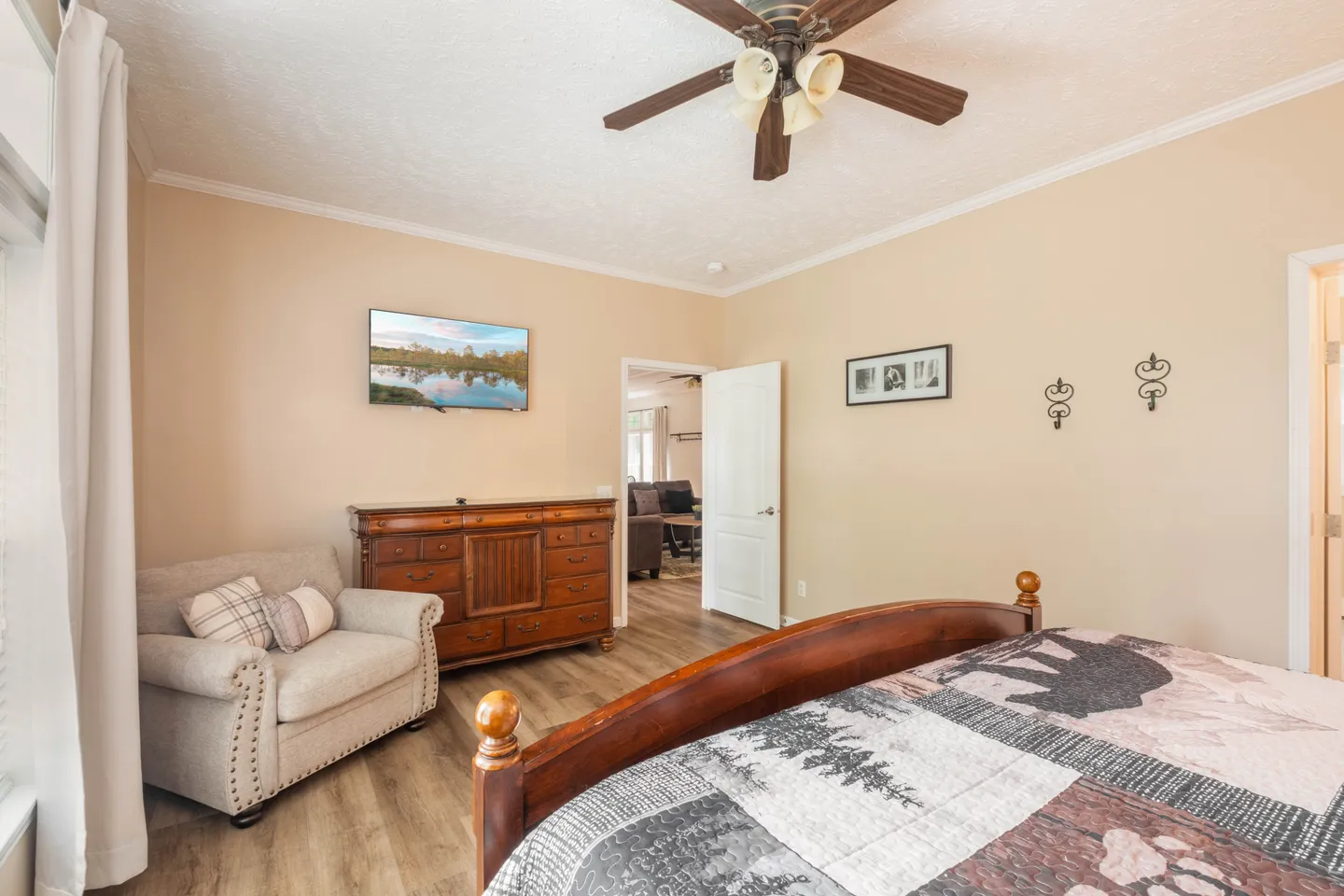 Bedroom featuring a wooden bed frame with a bear-themed quilt, an armchair, a wooden dresser, a wall-mounted TV, and an overhead ceiling fan.