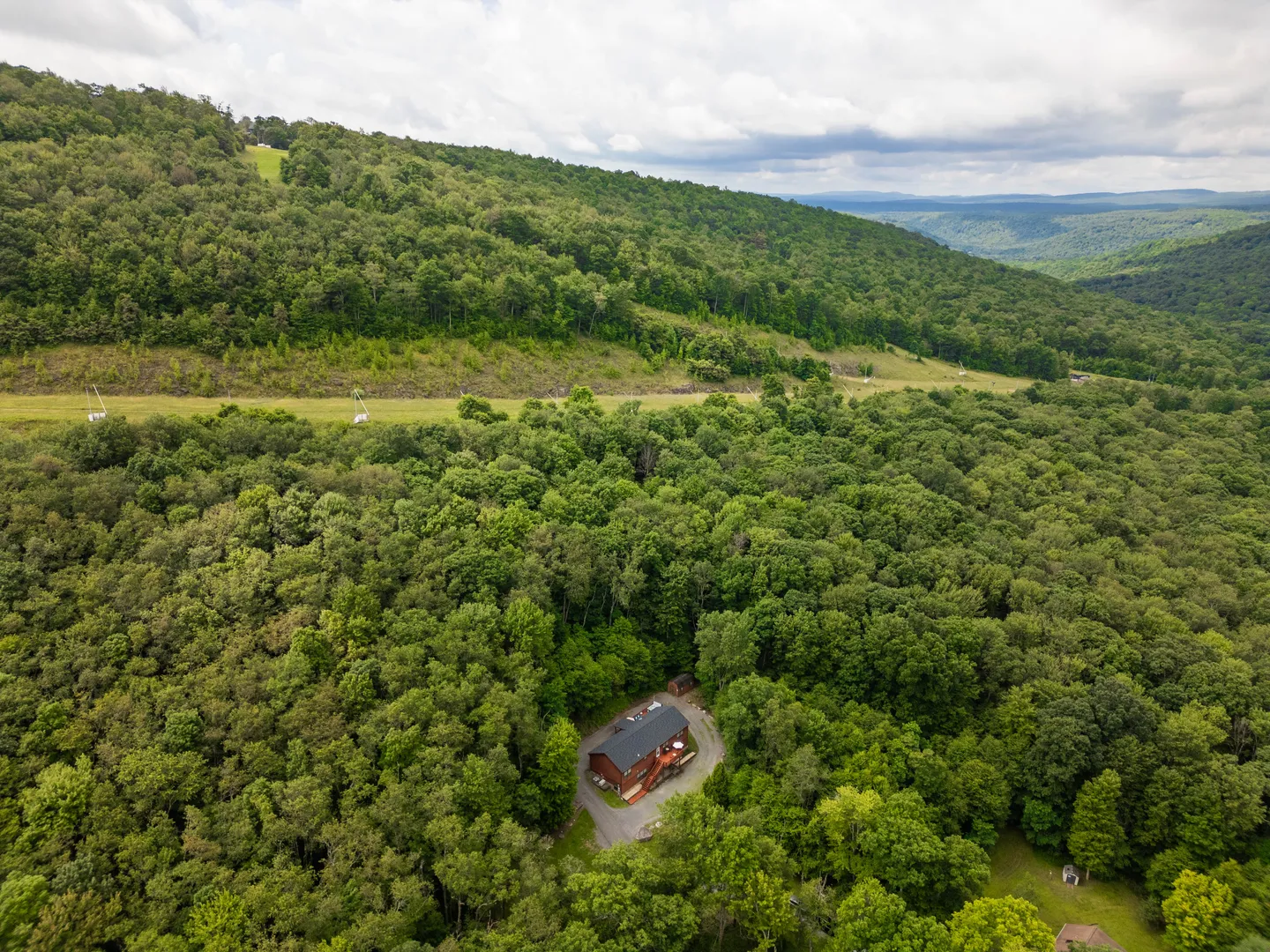 Aerial view of a secluded mountain home surrounded by dense forest near rolling hills and ski runs.