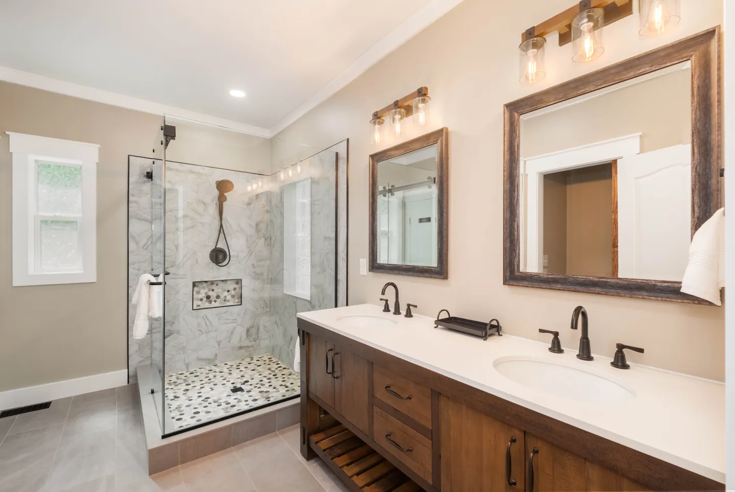 Bathroom with a double sink vanity, two wood-framed mirrors, and a glass-enclosed walk-in shower with stone tile.