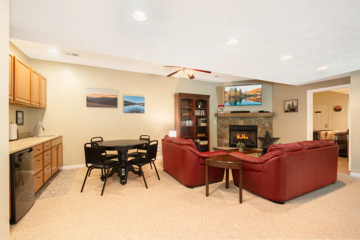 Finished basement living area with red leather couches, a stone corner fireplace, TV, wet bar, and a small dining table.