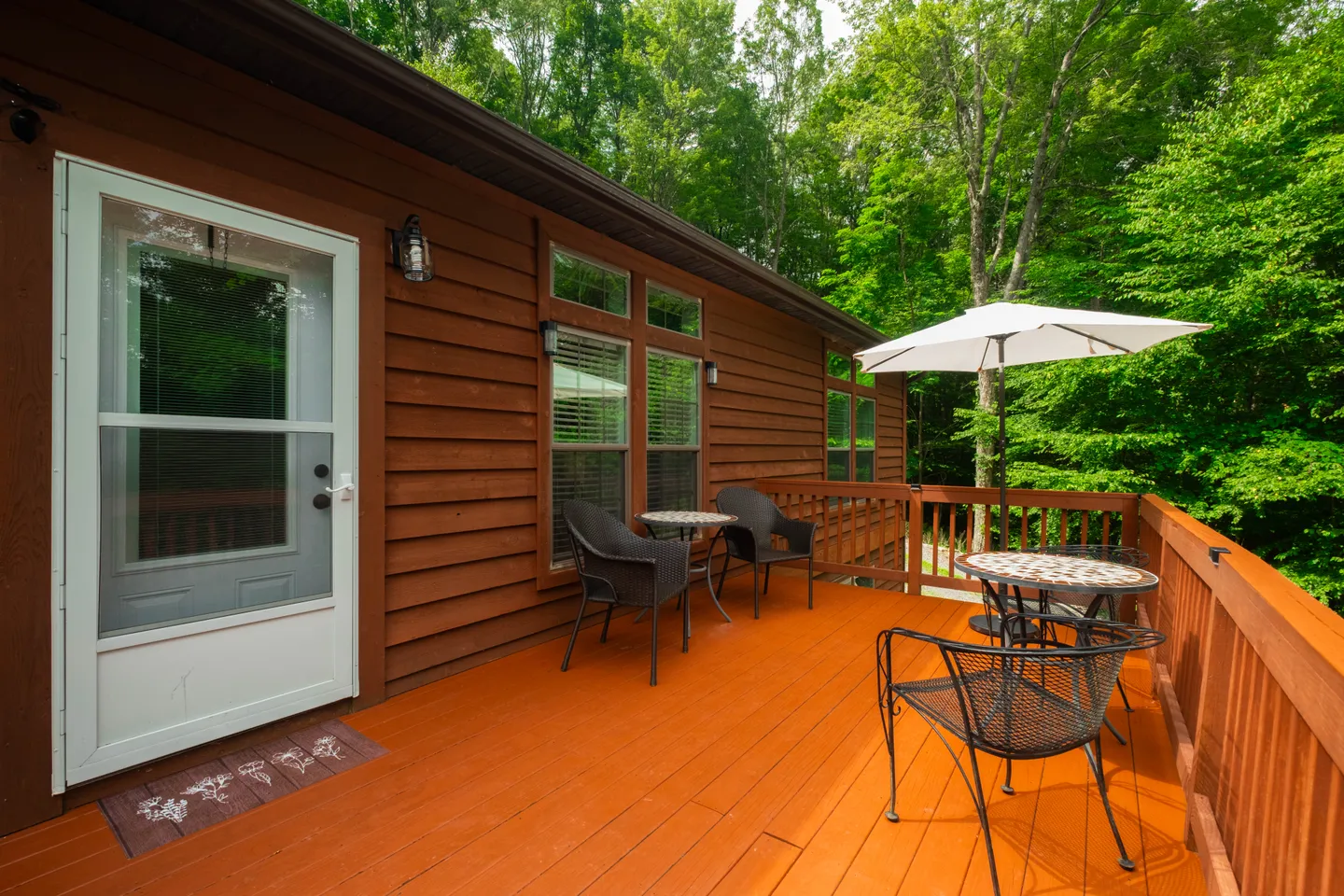 Outdoor wood deck alongside a brown log-style cabin with patio seating and a white umbrella.
