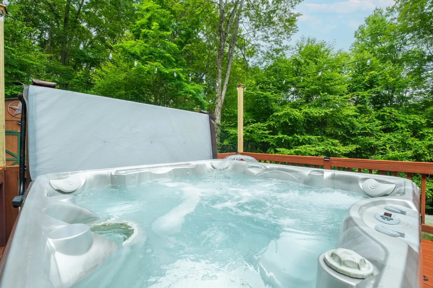 Outdoor hot tub filled with bubbling water on an open wooden deck surrounded by green trees.