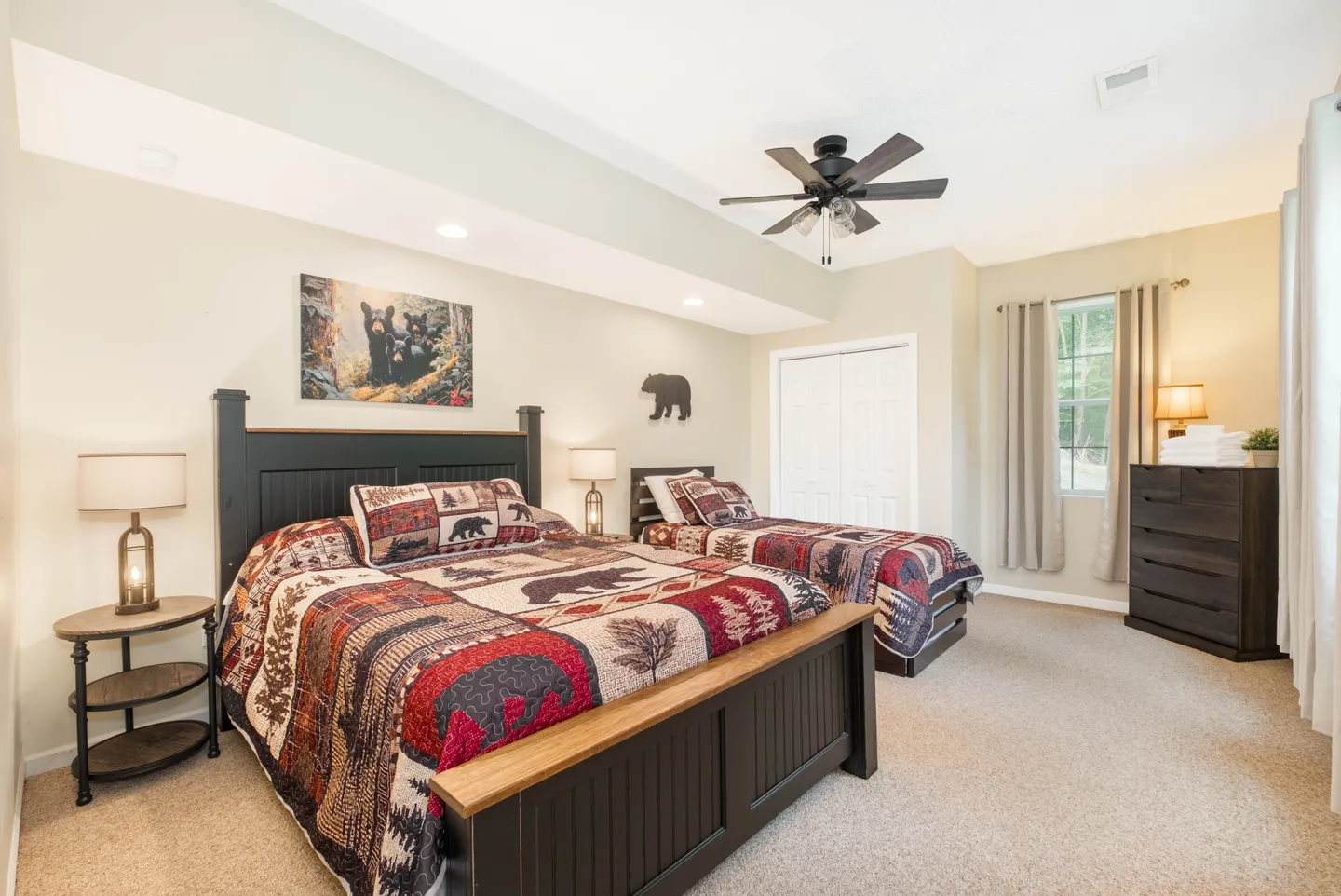 Bedroom with two beds topped with rustic bear-patterned quilts, bedside lamps, a ceiling fan, and carpeted flooring.