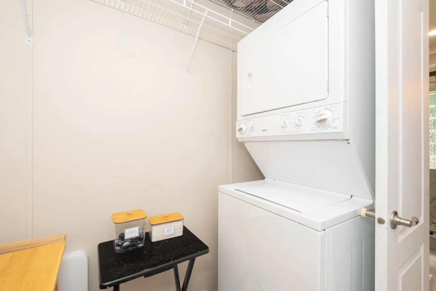 A stacked white washer and dryer unit inside a laundry closet with a wire shelf above.