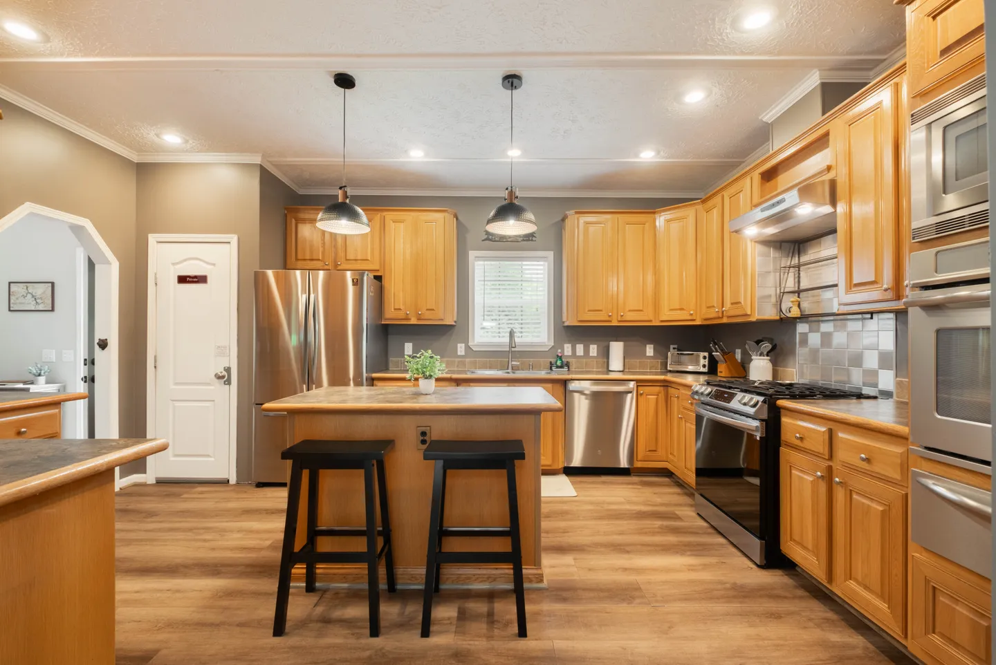 Kitchen with light wood cabinets, stainless steel appliances, and a central island with two black stools.