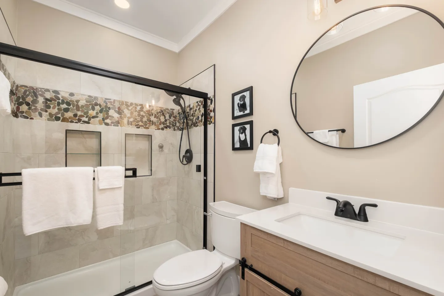 Bathroom featuring a walk-in shower with sliding glass doors, pebble accent tile, toilet, and vanity with circular mirror.