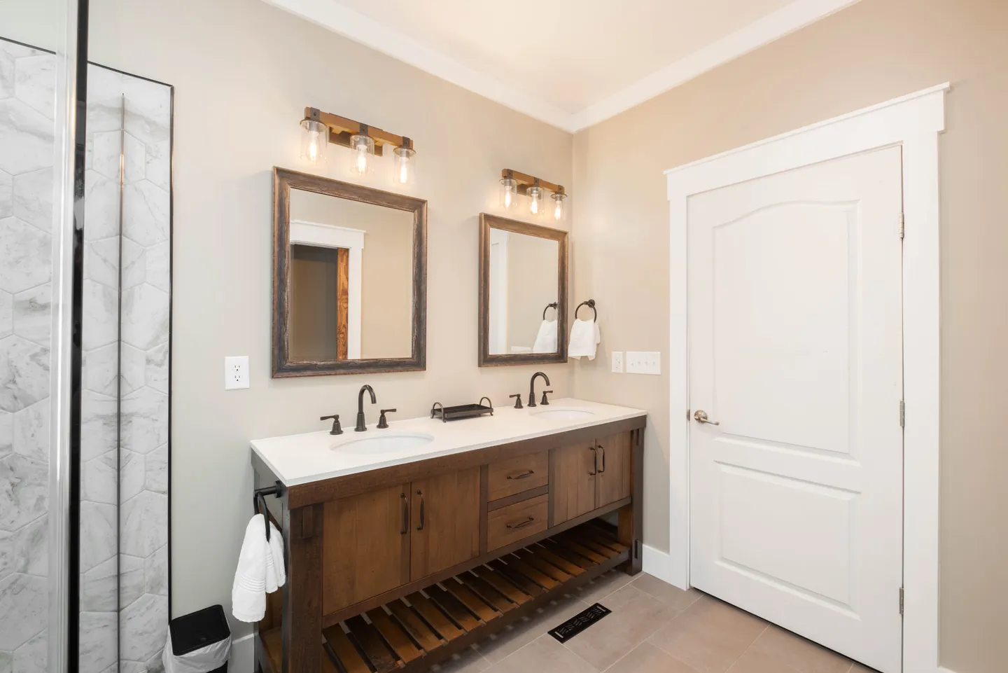Bathroom with a double-sink dark wood vanity, white countertop, two framed mirrors, and glass shower door on the left.
