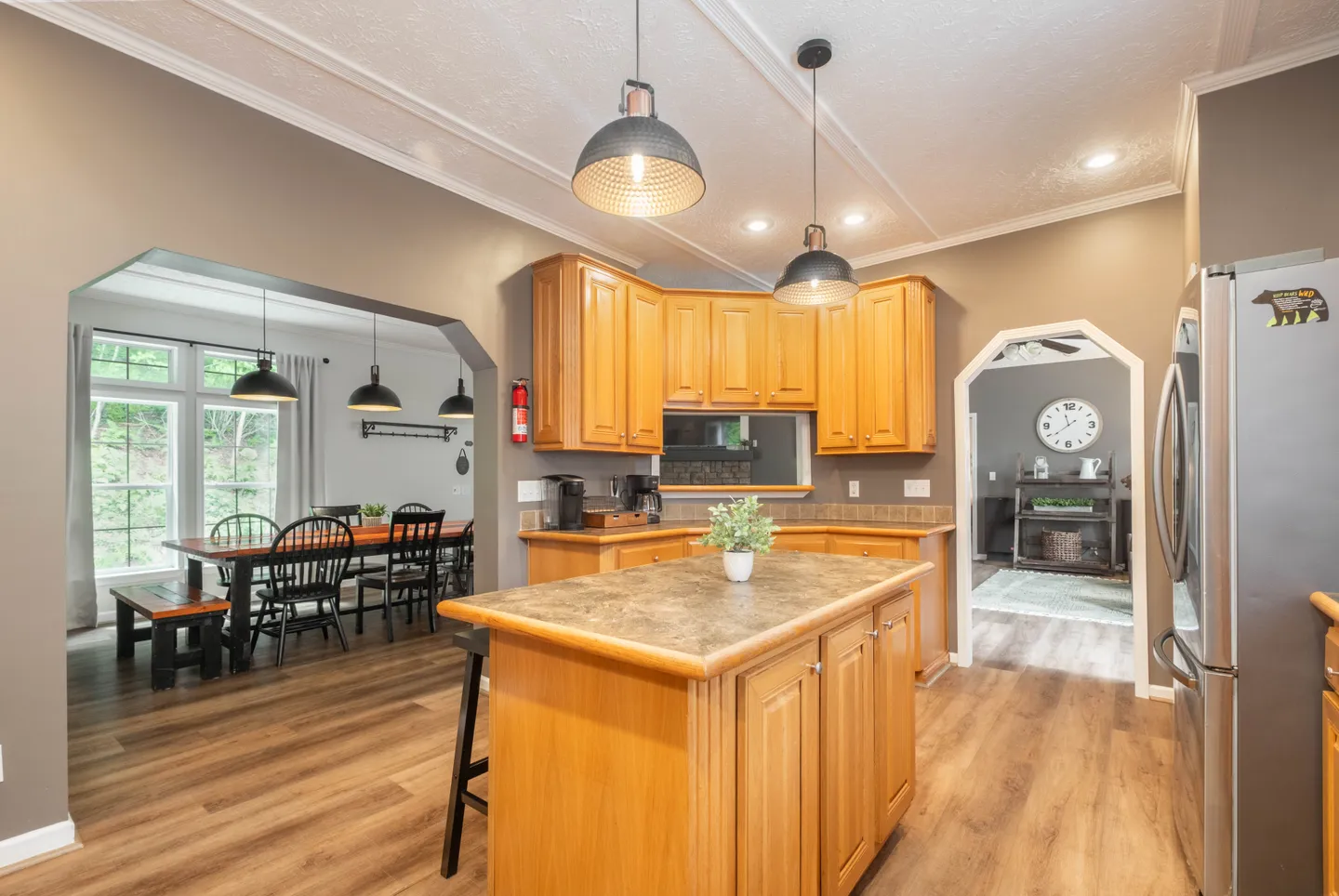 Kitchen with wooden cabinets and a central island opening into an adjacent dining area.