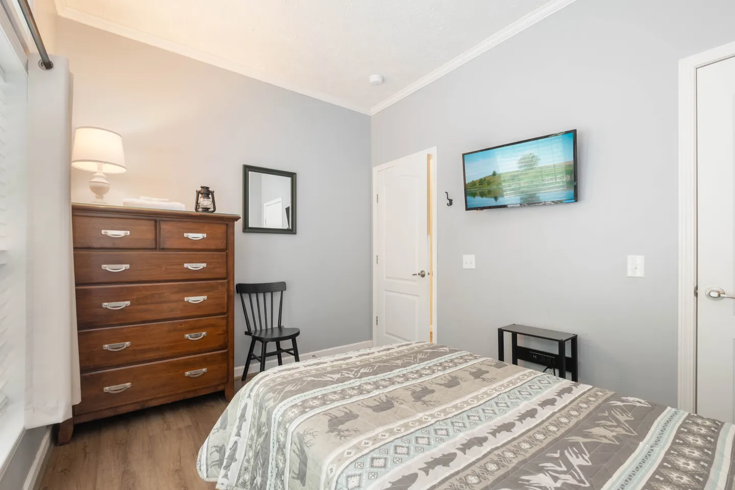 Bedroom featuring a bed with a wildlife-patterned quilt, wooden dresser, wall-mounted television, and wood-look flooring.