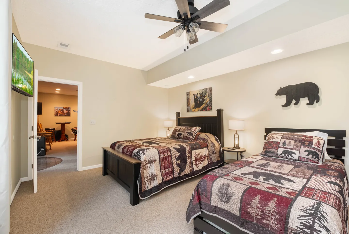Bedroom featuring two dark wood beds with rustic bear and pine tree quilts, carpeted floors, and a ceiling fan.
