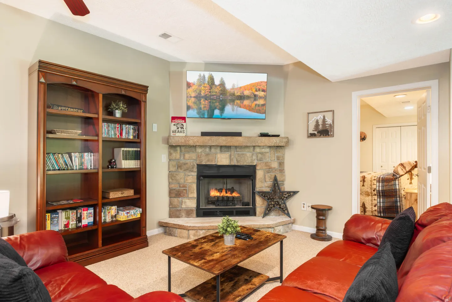Living area with a corner stone fireplace, wall-mounted TV, red leather seating, and a tall wooden bookcase.