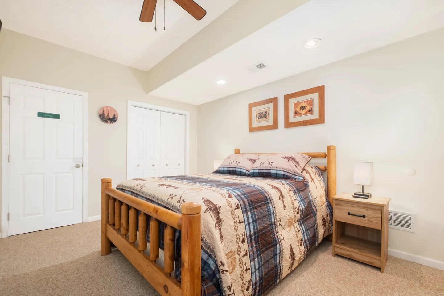 Bedroom featuring a log-style wooden bed, a nightstand with a lamp, carpeted flooring, and framed wildlife artwork.