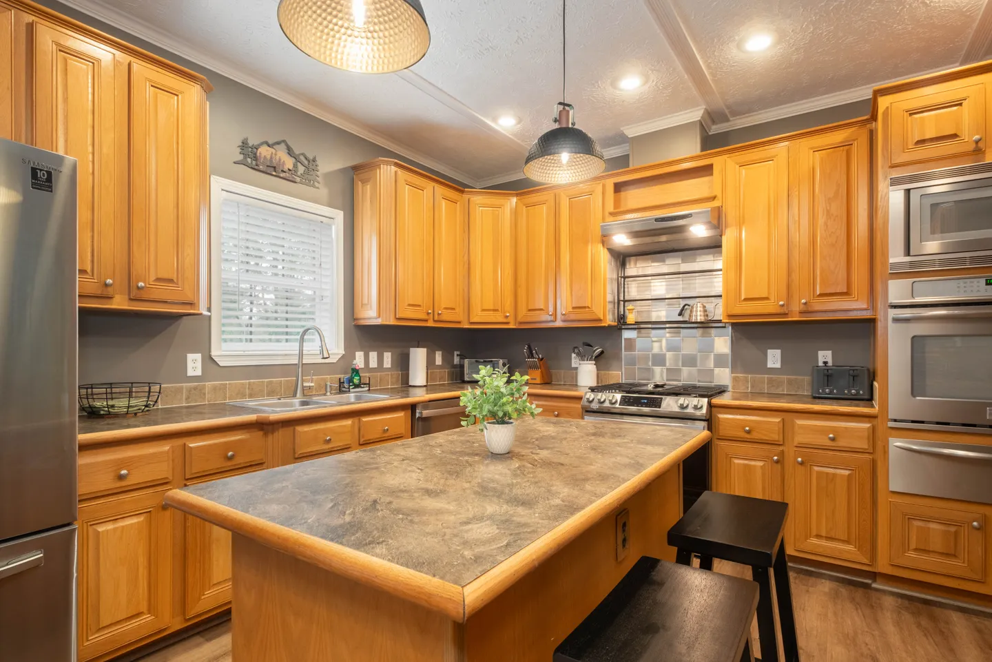 A kitchen with wood cabinets, dark countertops, an island with bar stools, and stainless steel appliances.