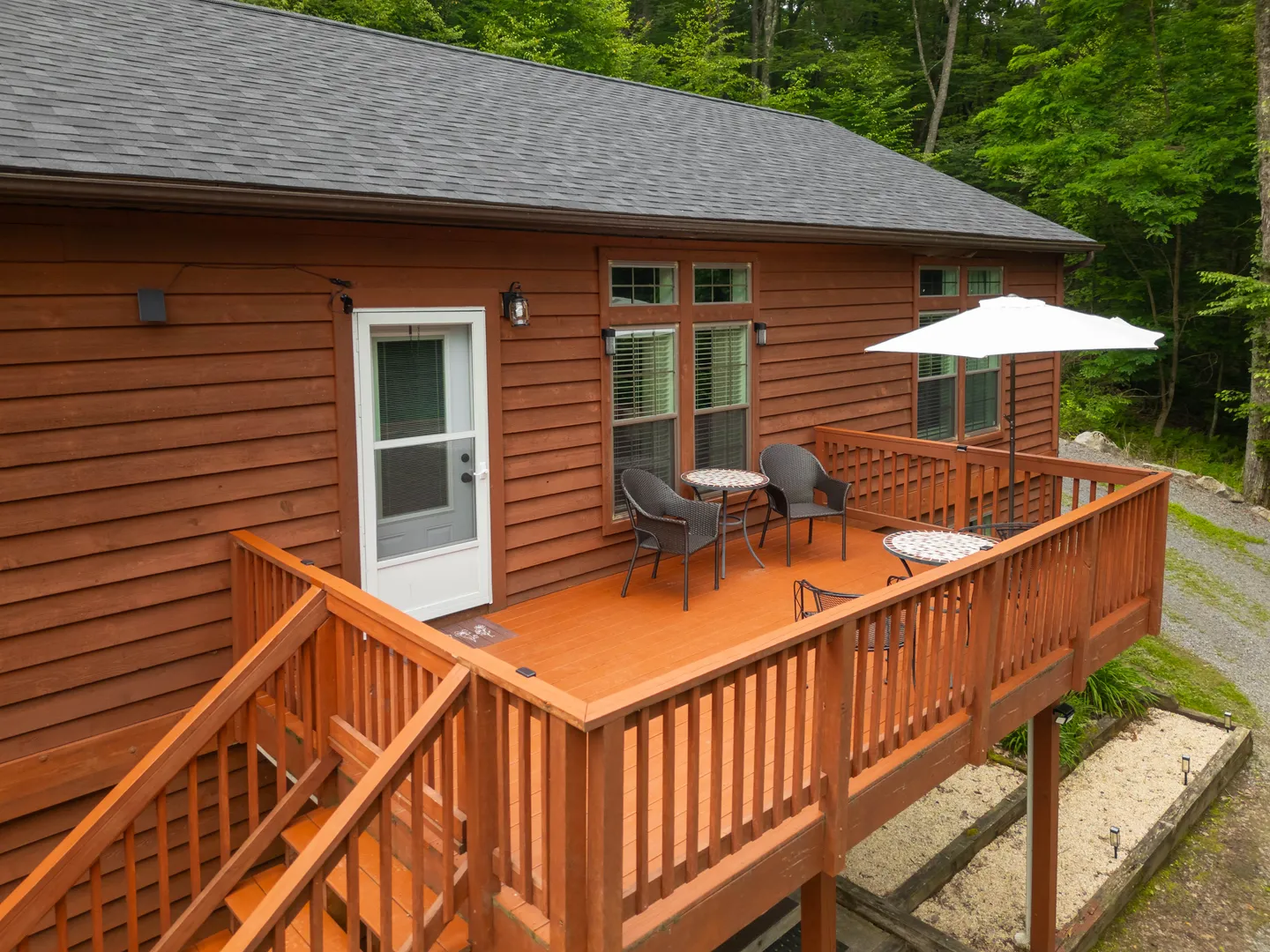 Elevated wooden deck with outdoor patio tables, chairs, and an umbrella outside a wood-sided cabin.