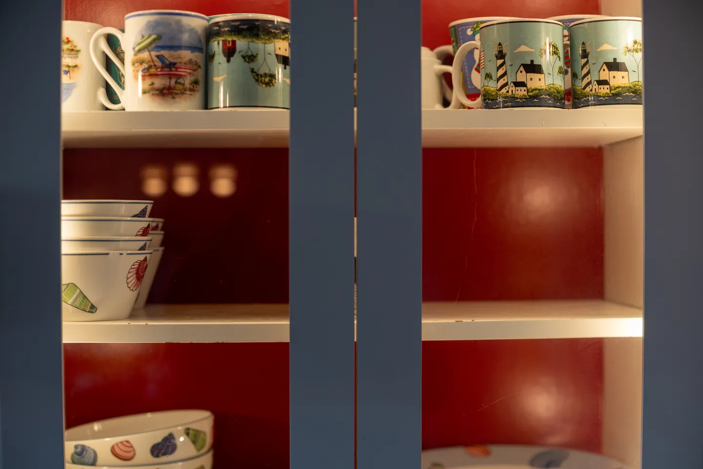 Open cabinet shelves revealing beach-themed mugs and bowls set against a red interior wall.