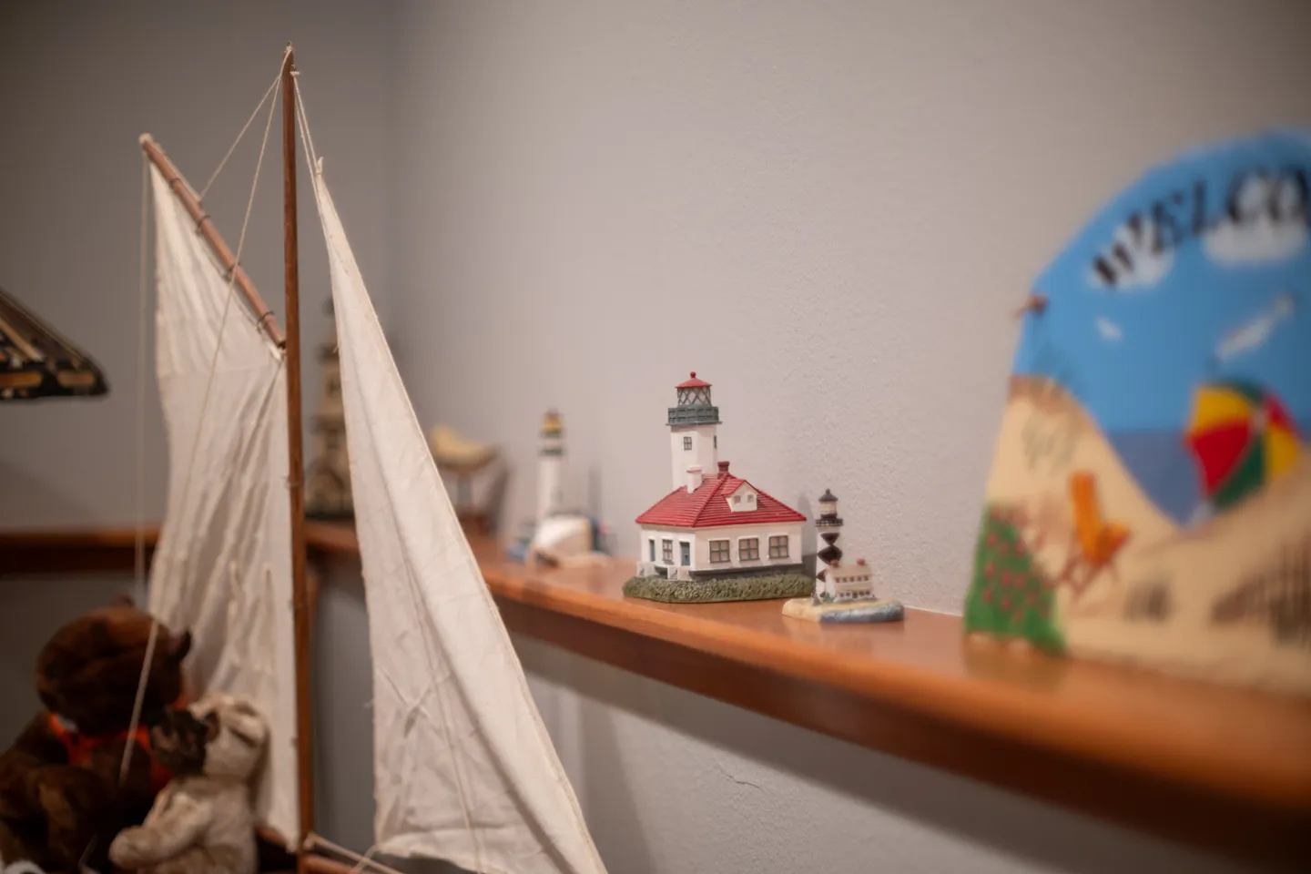 Close-up of decorative items including lighthouse figurines, a model sailboat, and a welcome sign along a wooden wall ledge.