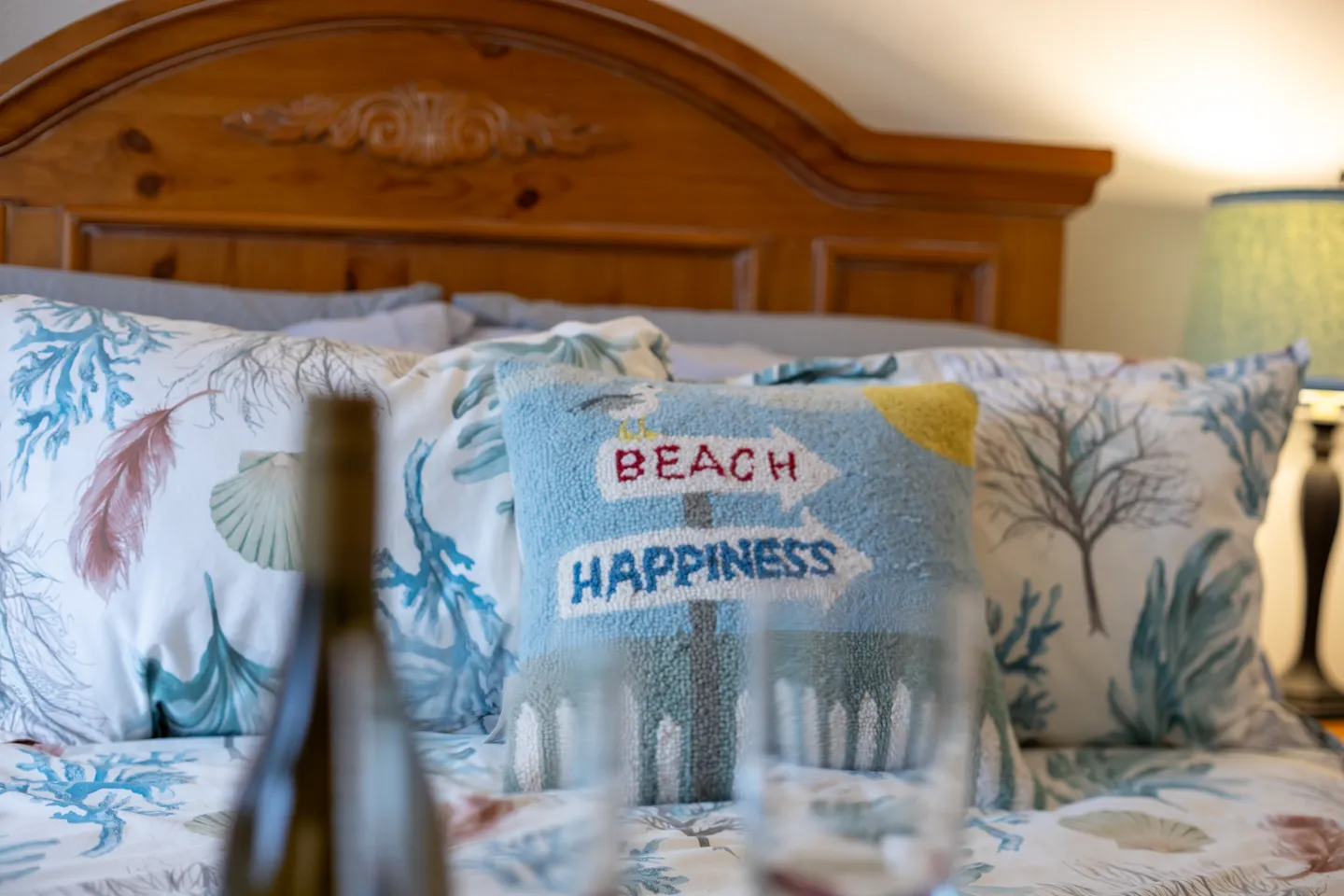 Close-up of a bed with a wooden headboard, coastal-patterned pillows, and a small decorative pillow reading Beach Happiness.