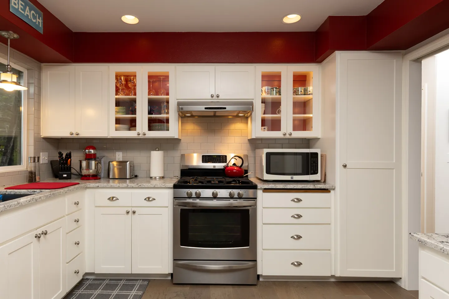 Kitchen with white cabinetry, speckled granite-look countertops, stainless steel gas range, and red accent trim above the upper cabinets.