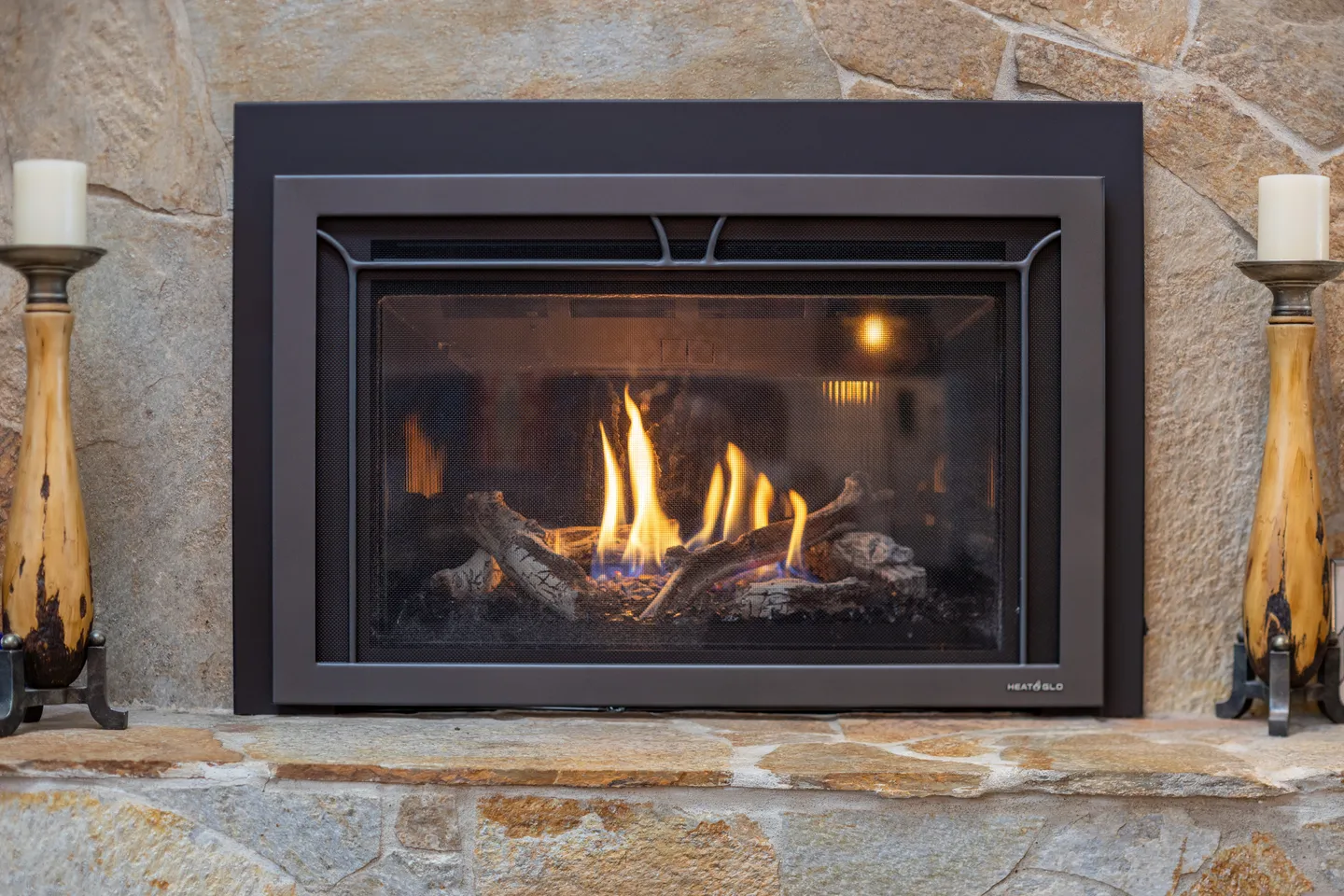 Close-up view of a lit gas fireplace with artificial logs set into a stone hearth.