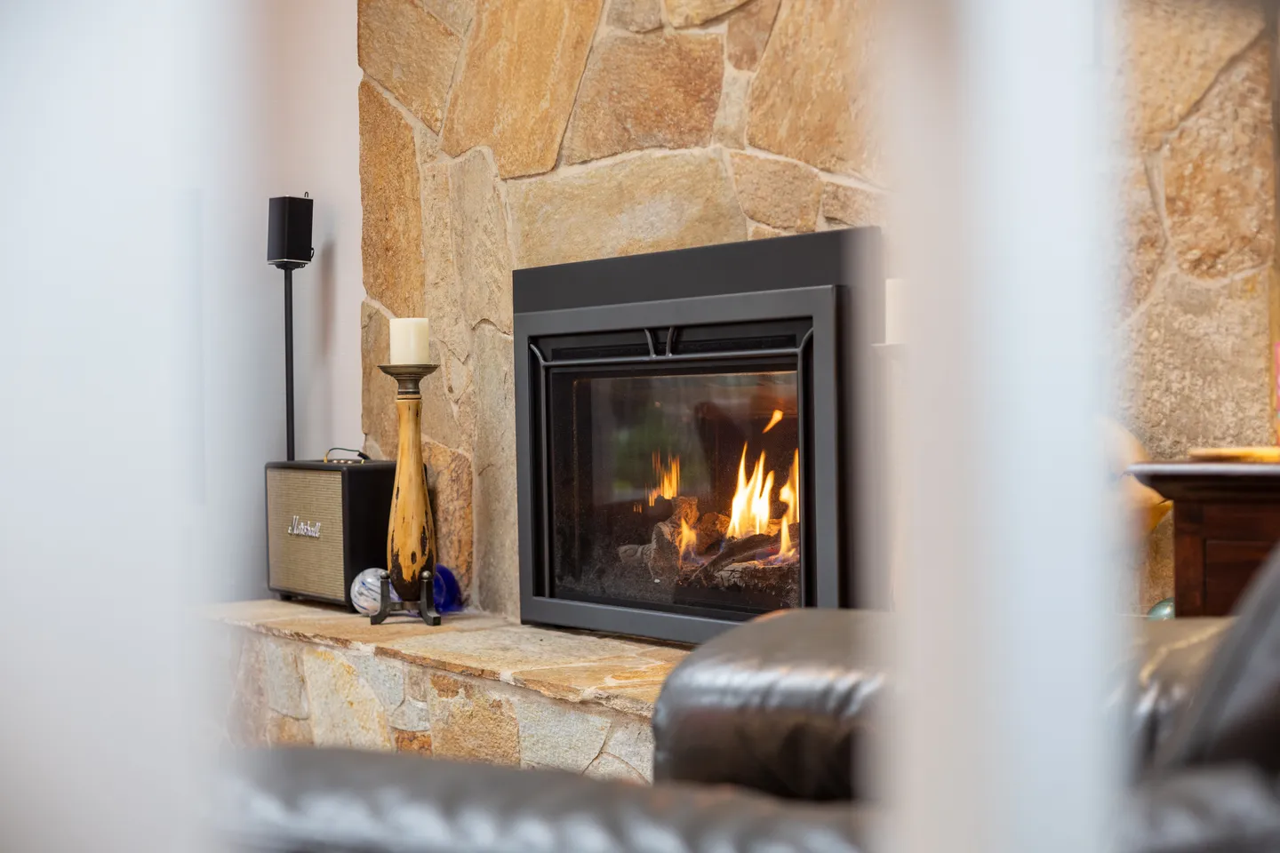 Close-up of a modern black glass-front fireplace surrounded by a rustic tan stone wall and raised hearth.