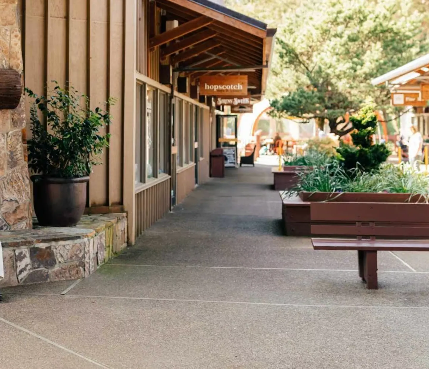 Outdoor pedestrian walkway lined with storefronts, benches, and landscaping planters.