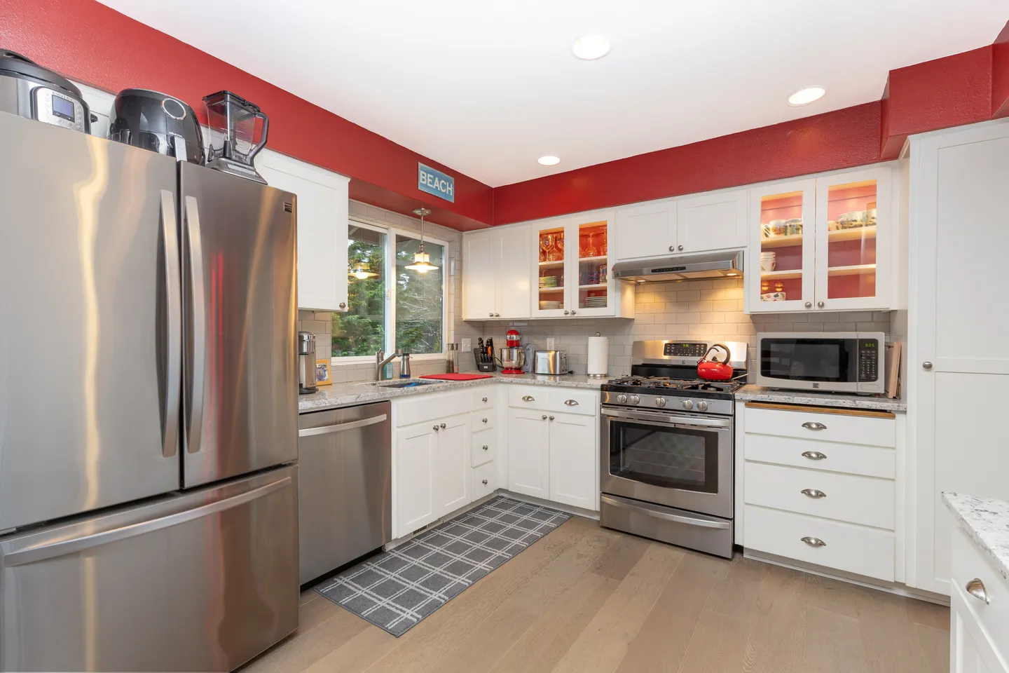 Kitchen with white cabinetry, red upper wall accent, stainless steel appliances, and a window above the sink.