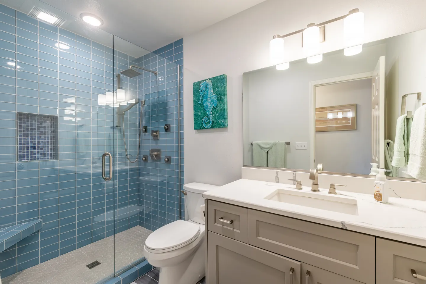 Bathroom featuring a walk-in shower with light blue tile, a glass door, a modern vanity, and a seahorse painting.