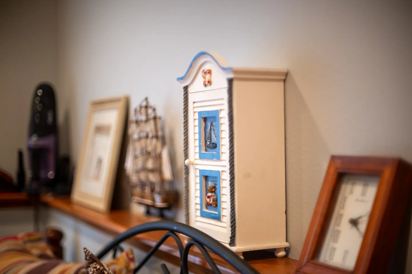 Close-up of decorative items on a shelf including a miniature nautical cabinet, framed picture, model sailboat, and clock.