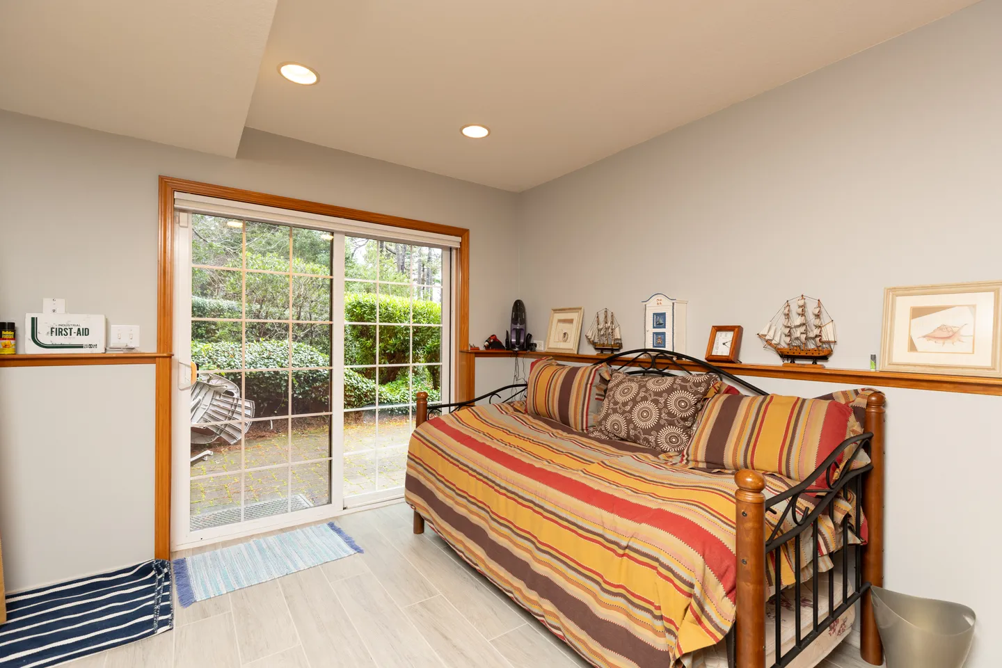 A daybed with striped bedding set along a wall with a display ledge, adjacent to sliding glass doors opening to an outdoor patio.