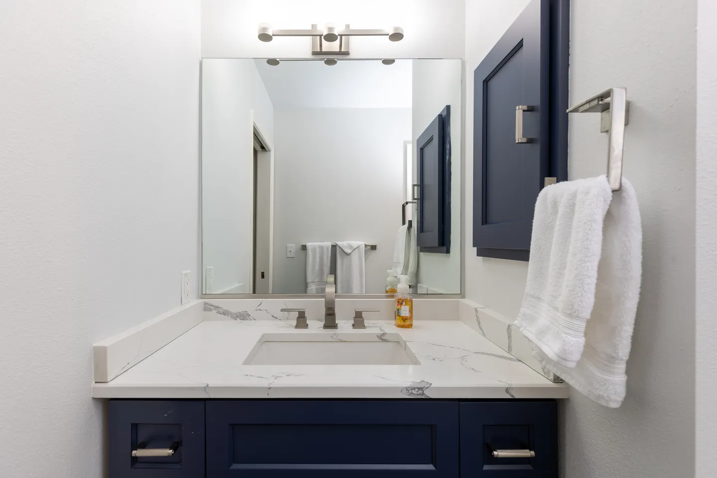 Bathroom vanity with a dark blue cabinet, white marble-patterned countertop, rectangular undermount sink, and a large mirror.