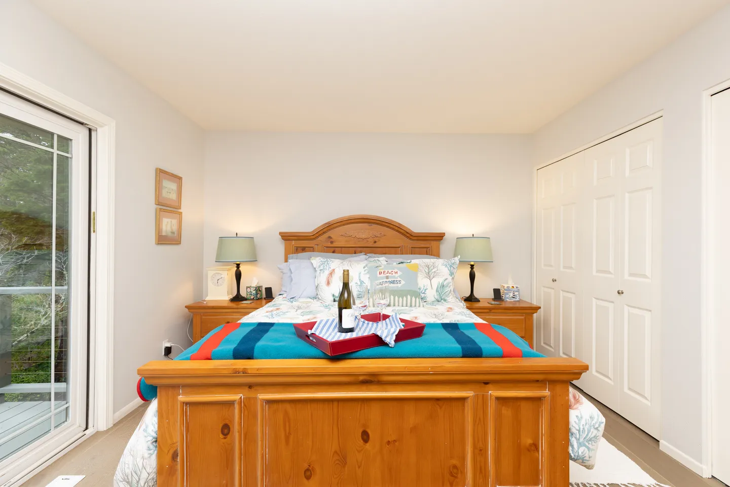 Bedroom featuring a wooden bed frame, matching nightstands with lamps, white closet doors, and a sliding glass door leading outside.