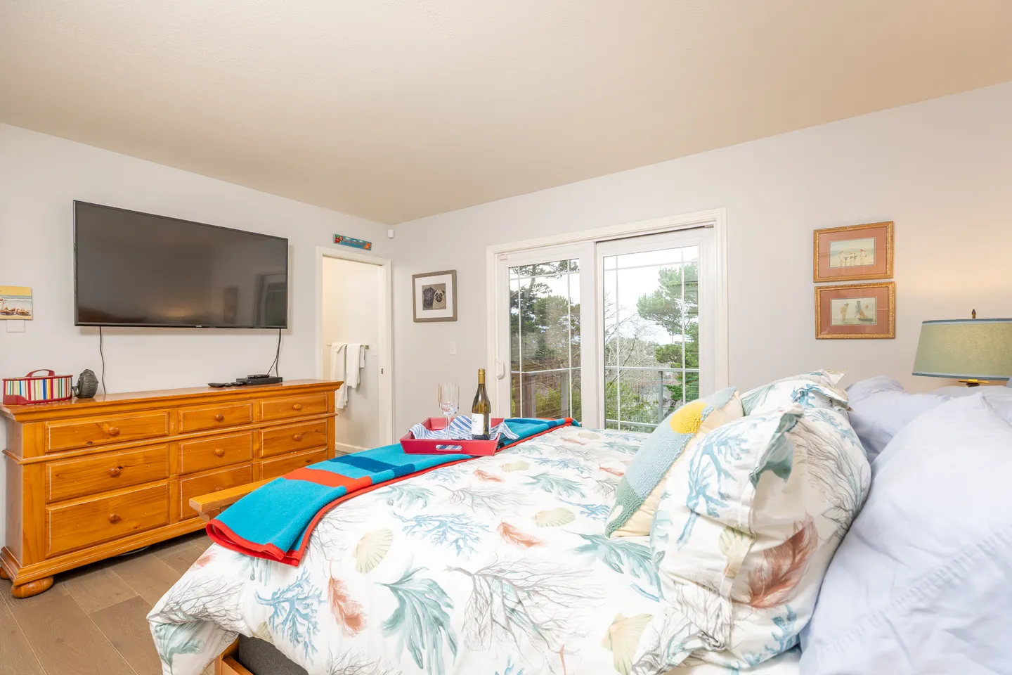 Bedroom featuring a bed with coastal-themed bedding, a wooden dresser with a wall-mounted TV, and sliding glass doors.