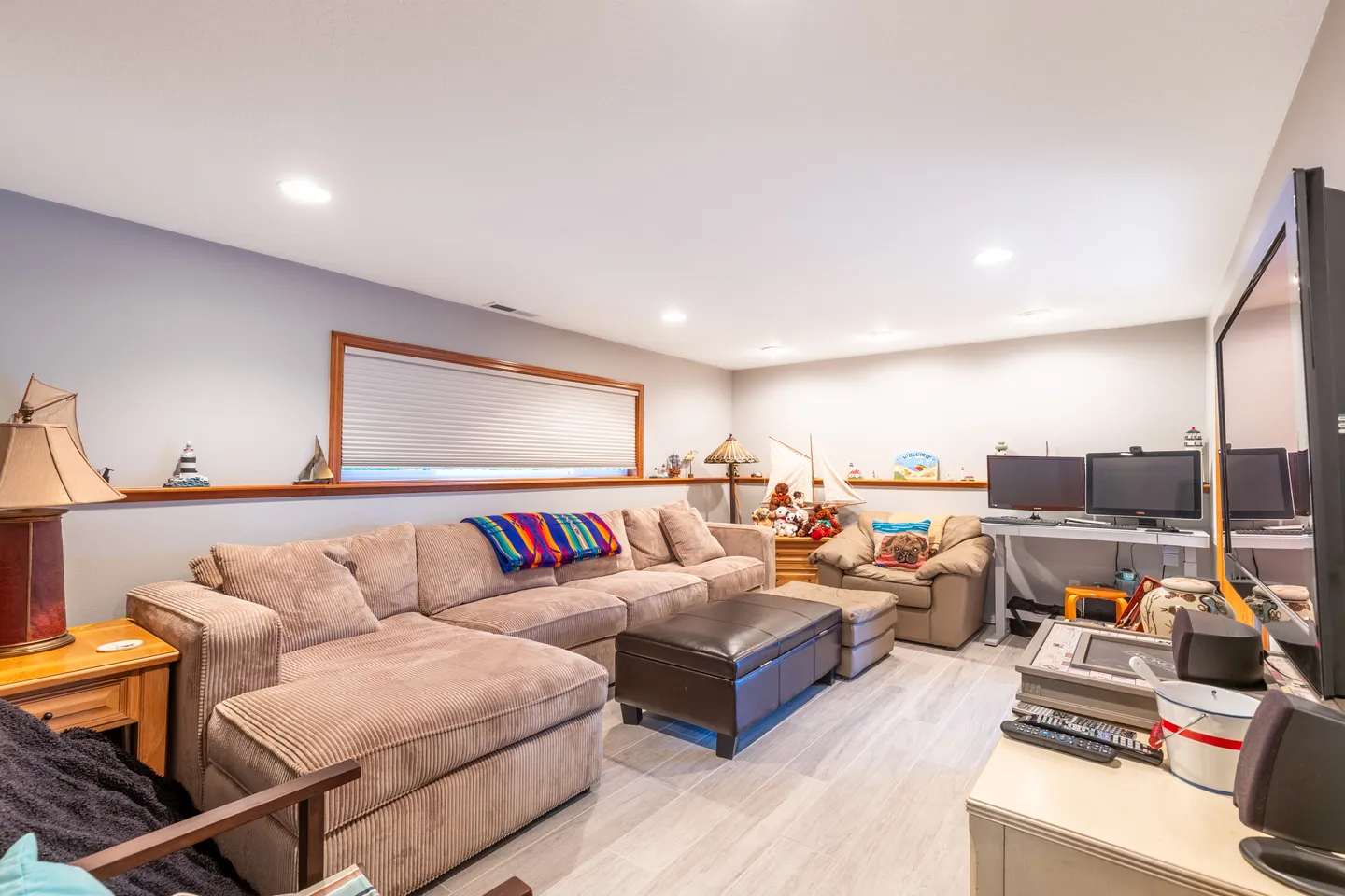 Living area with a large corduroy sectional sofa, leather ottoman, TV, and computer desk setup.